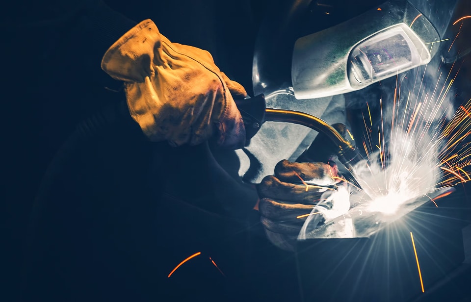 Soudure professionnelle : la puissance de l'arc électrique. Soudeur professionnel en gros plan, portant un masque et des gants de cuir, générant un arc électrique intense et des étincelles vives.